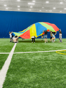 Kids playing organized field games on indoor turf during birthday party at Milwaukee Yard, parachute