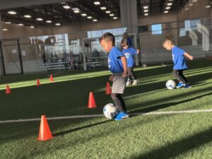Toddler dribbling through cones in a soccer drill during Mighty Tykes class
