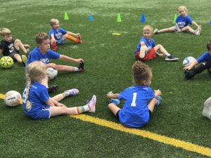 Mighty Tykes soccer coach leading toddlers through group stretching on indoor turf at Milwaukee Yard Oak Creek WI
